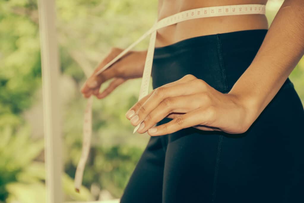 Mosolygó nő nagy nadrágot tart maga elé, a Saxenda gyártója által támogatott sikeres fogyás jelképeként.